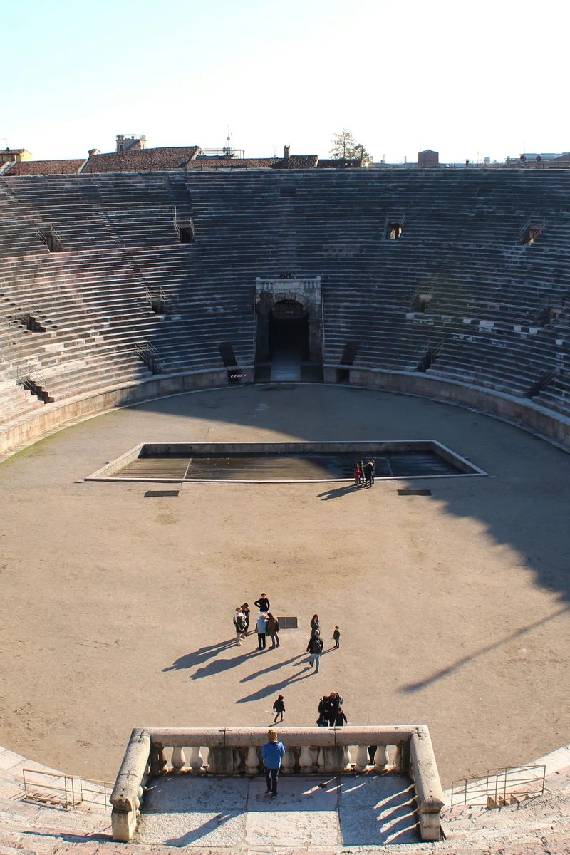 The Arena di Verona — the elliptical Roman amphitheatre in Piazza Bra, its pink-and-white limestone tiers rising against a clear Veronese sky